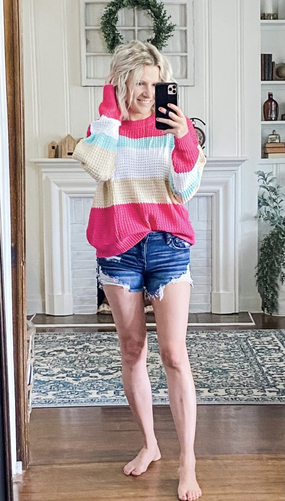 Woman wearing pink striped sweater and amazon ripped jean shorts